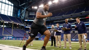 Large defensive tackle performing the 40-yard dash at the NFL Scouting Combine in front of scouts and coaches